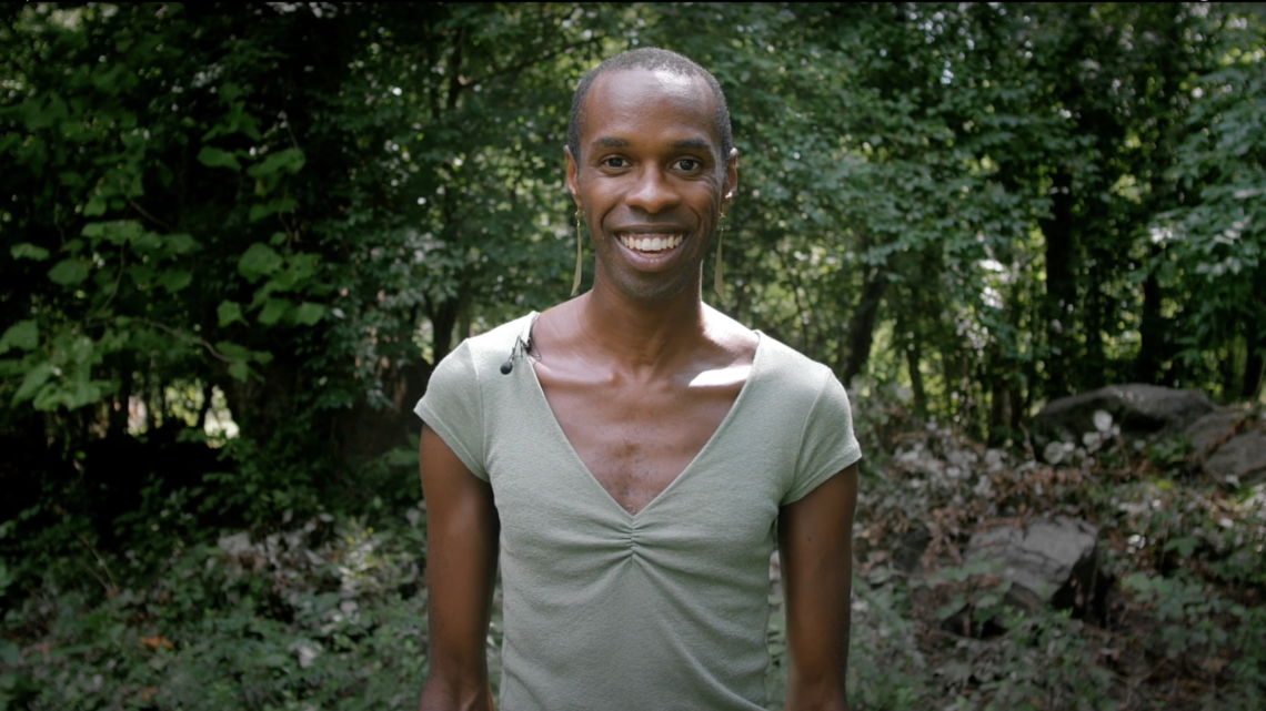 a smiling person in the center of the frame, standing in a forest