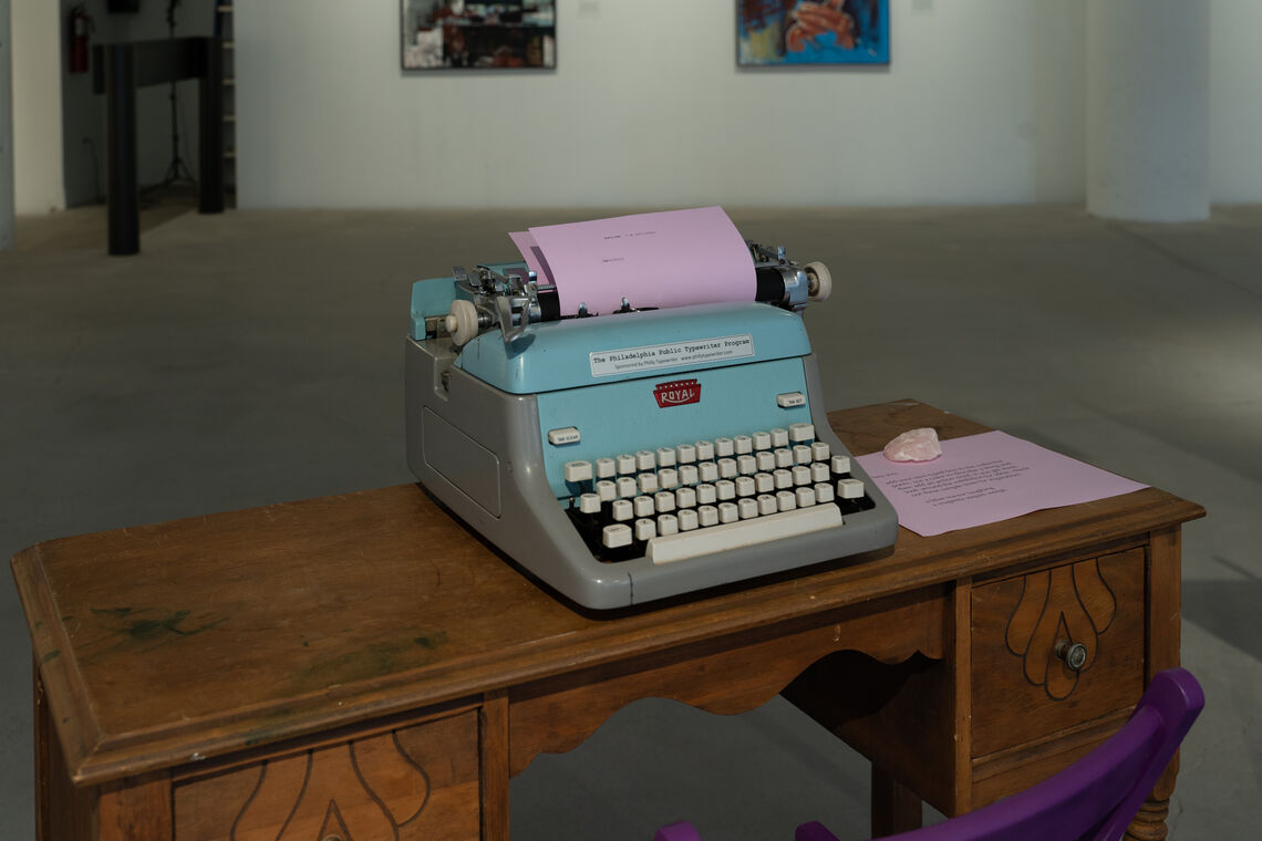 a typewriter with a sheet of paper in it, sitting on a wooden desk in the middle of a gallery