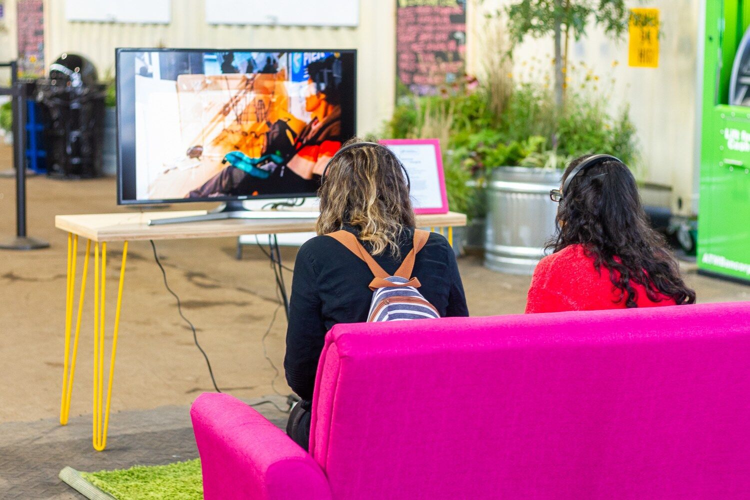 two people sitting on a pink couch watching a video screen