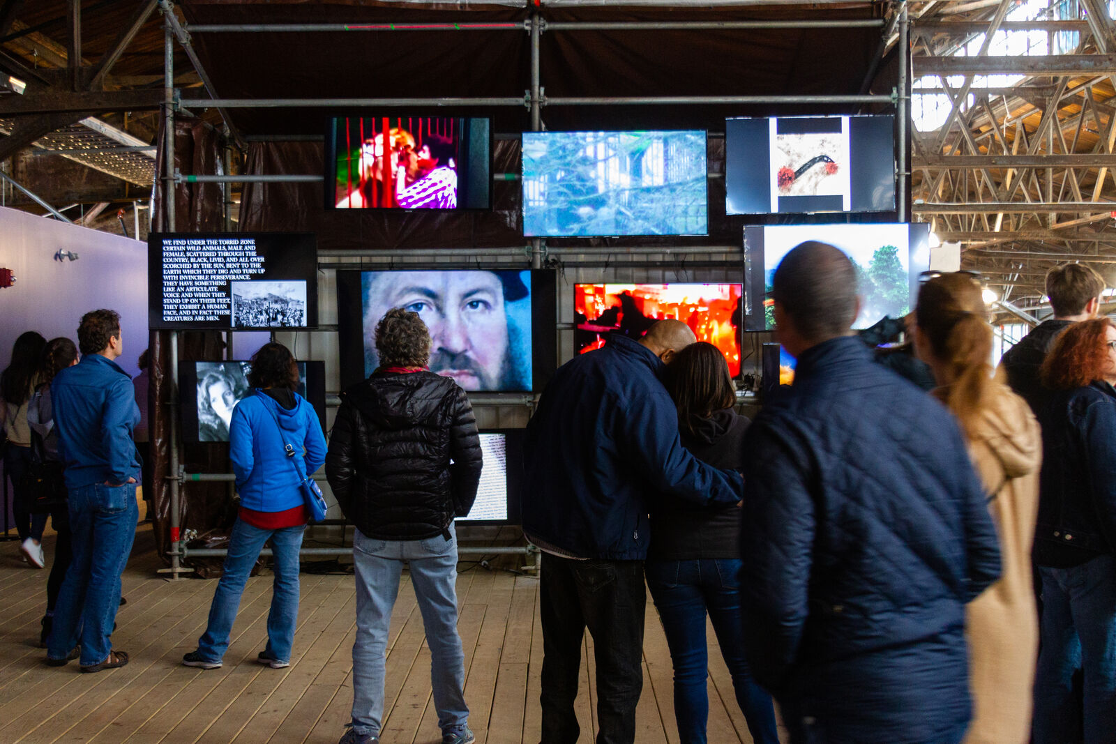 a crowd of people, all with their backs facing the camera. they're looking at a wall of screens, all with different images on them