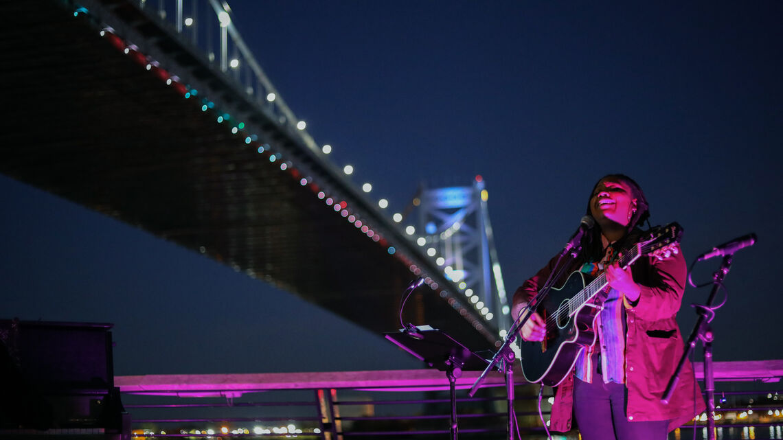 Person singing with guitar under Ben Franklin bridge