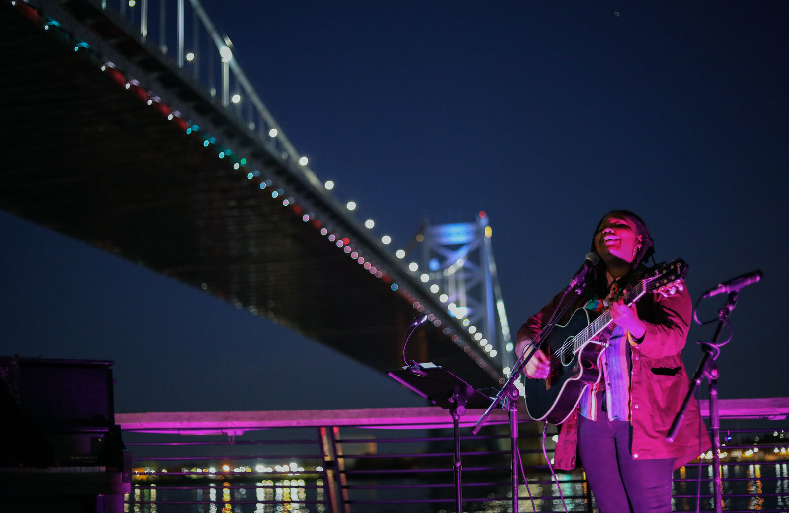 Person singing with guitar under Ben Franklin bridge