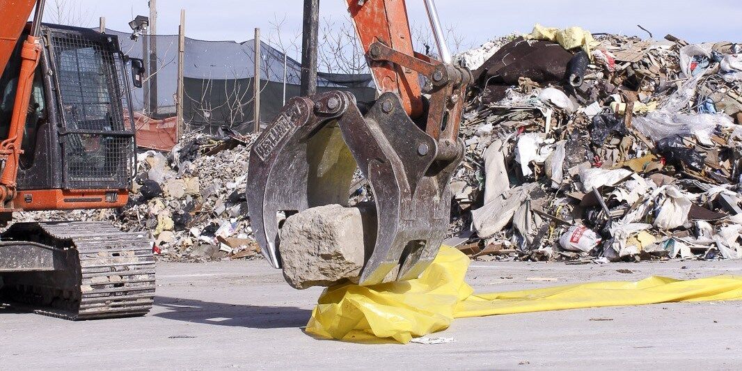 a forklift picking up a rock in front of a pile of trash