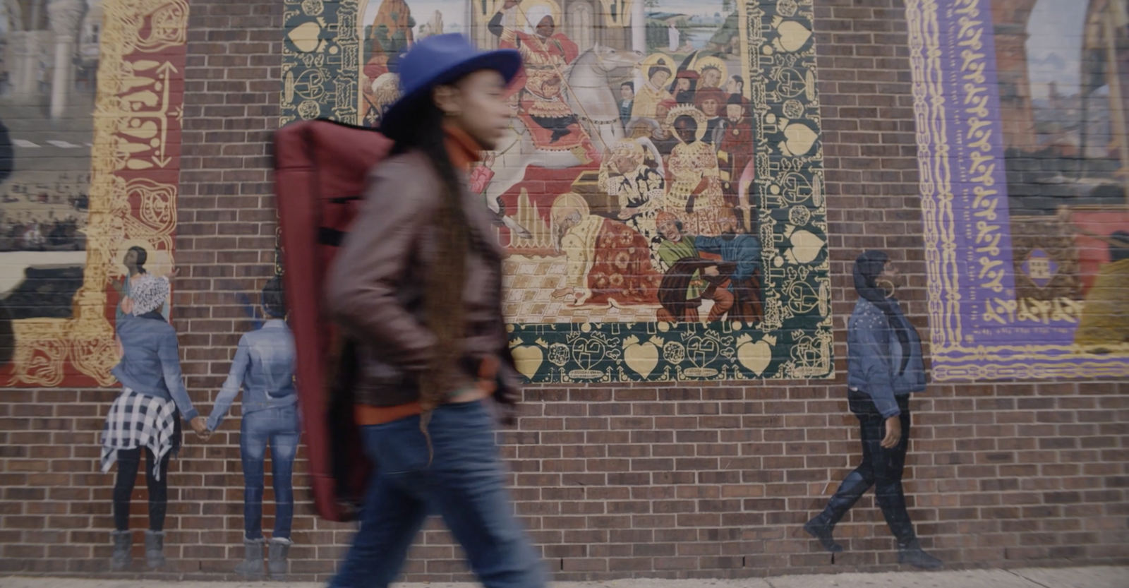 Person walking in front of a mural on a brick wall