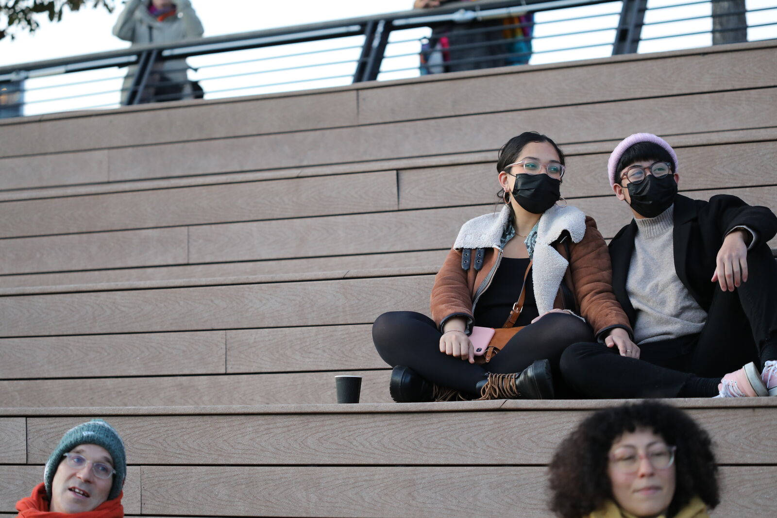 two masked audience members watch the performance from the bleachers