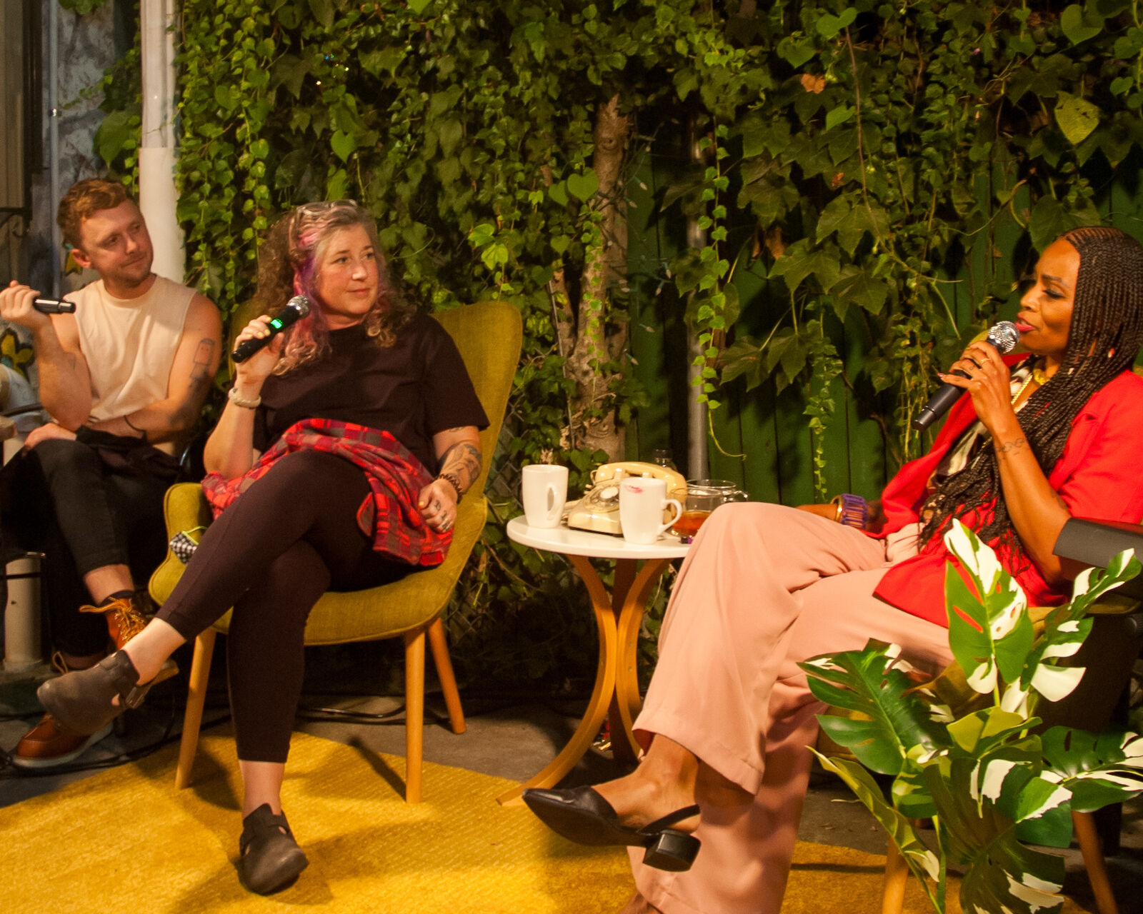 three people sit in front of wall of plants discussing things with landline telephone next to them