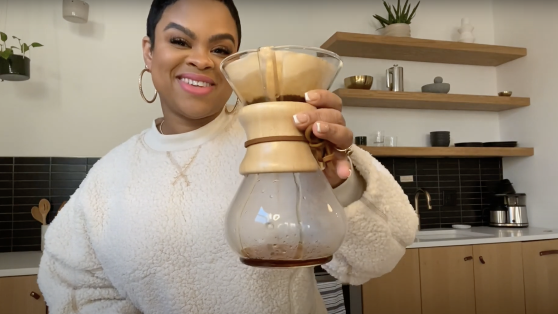woman holding a chemex coffee brewer in her kitchen smiling