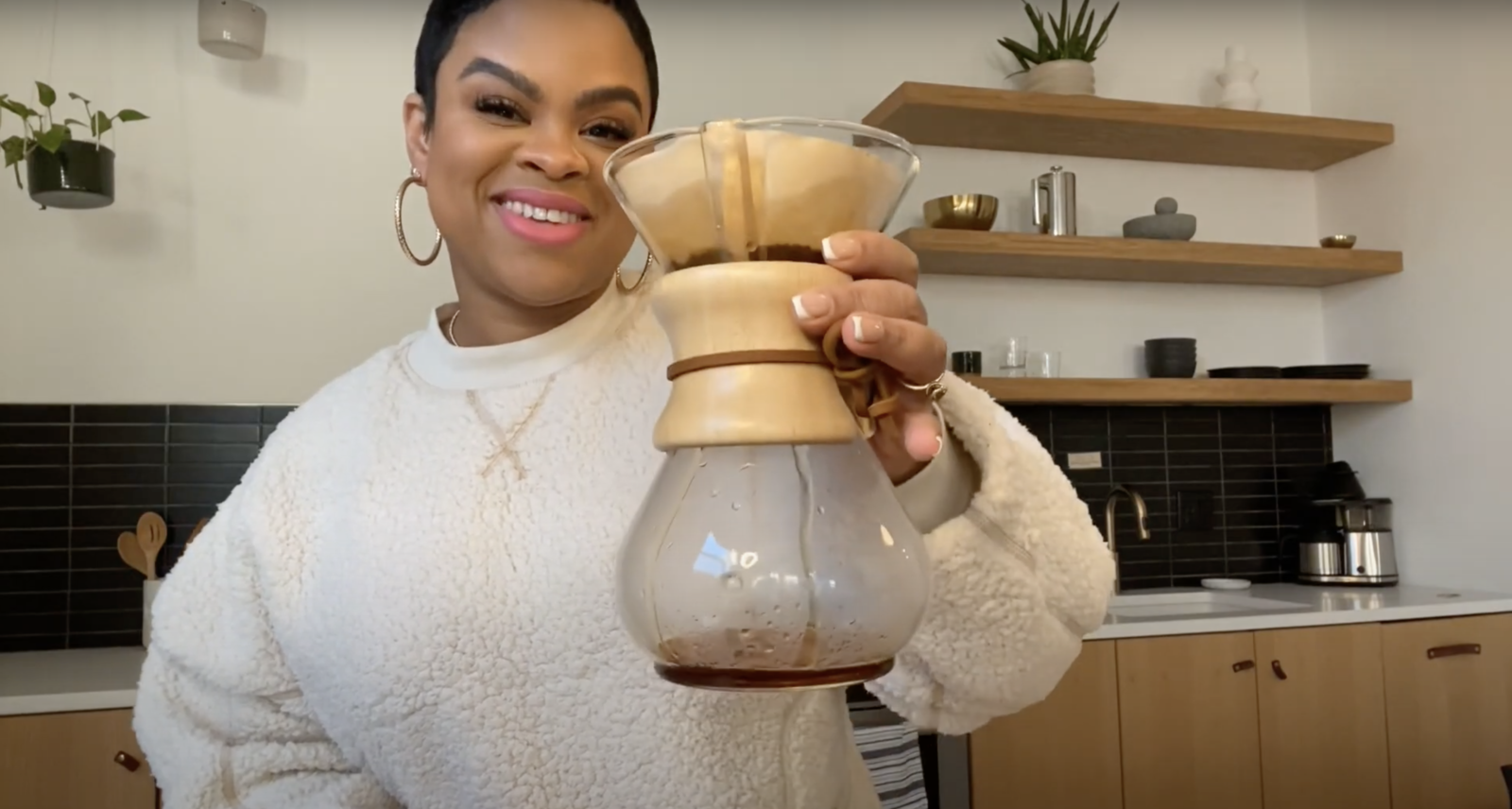 woman holding a chemex coffee brewer in her kitchen smiling