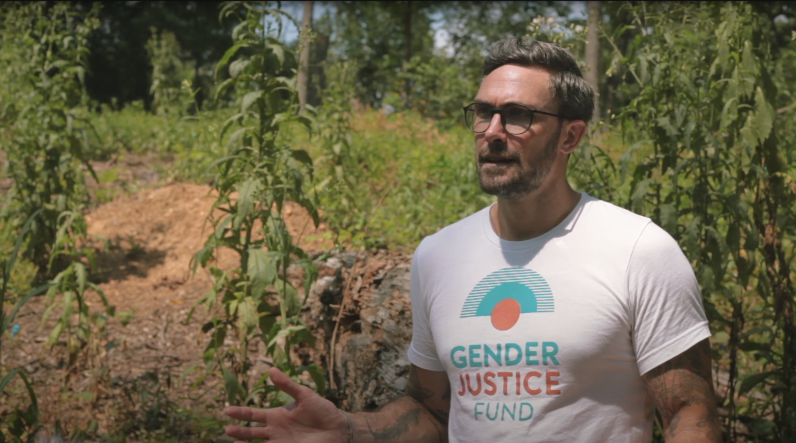 man with Gender Justice Fund tshirt with greenery in the background for 100 People Listening: Practicing Awareness When Listening project