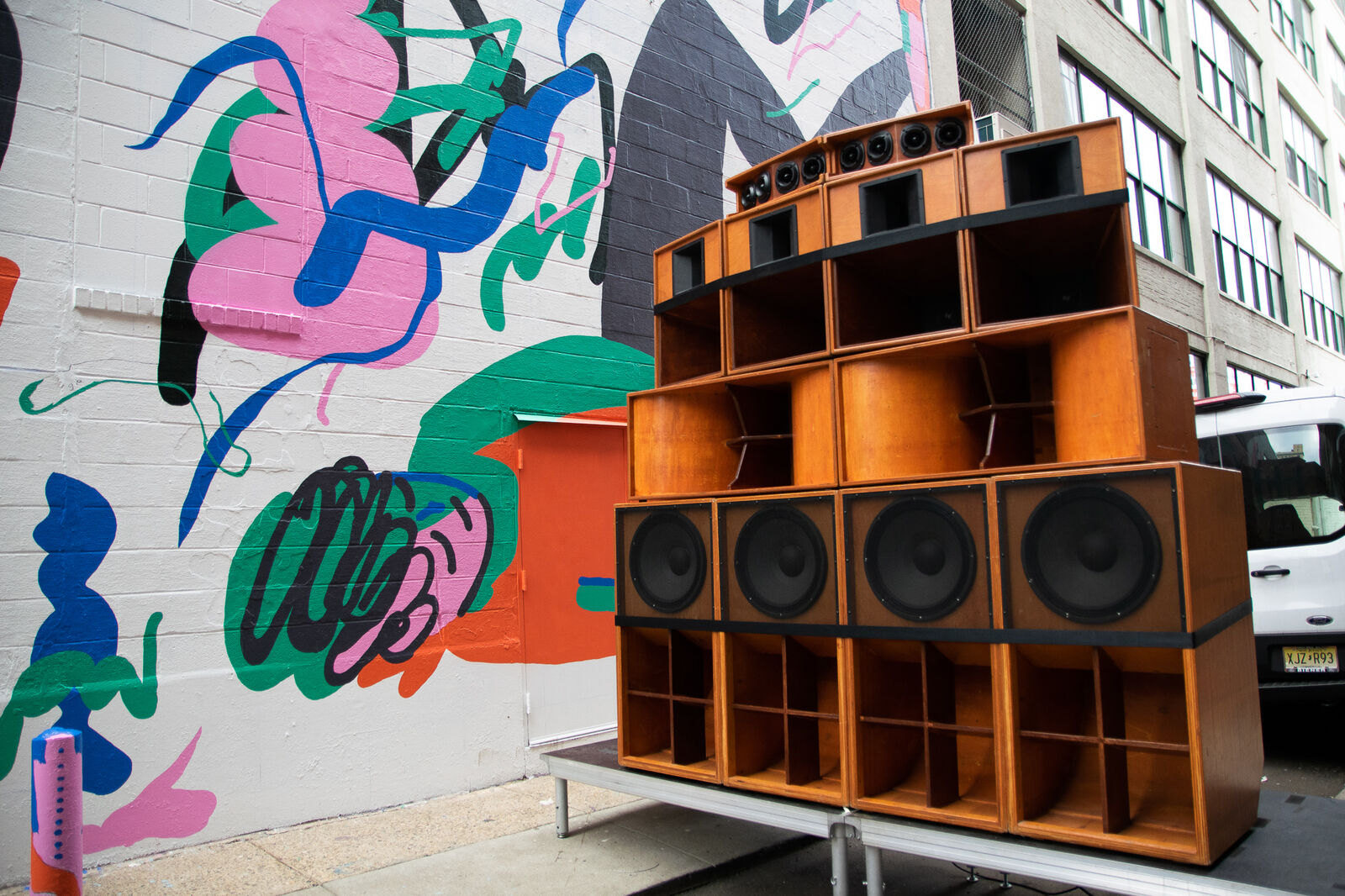wall of speaker cabinets in the street in front a colorful abstract mural