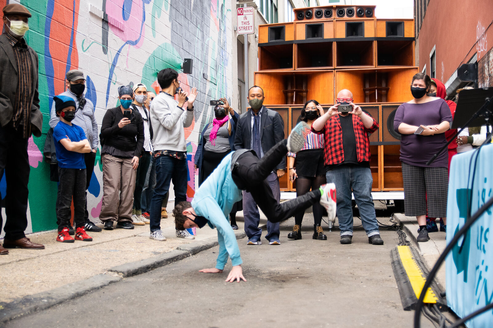 breakdancer in the streets in front of a wall of speaker cabinets and crowd