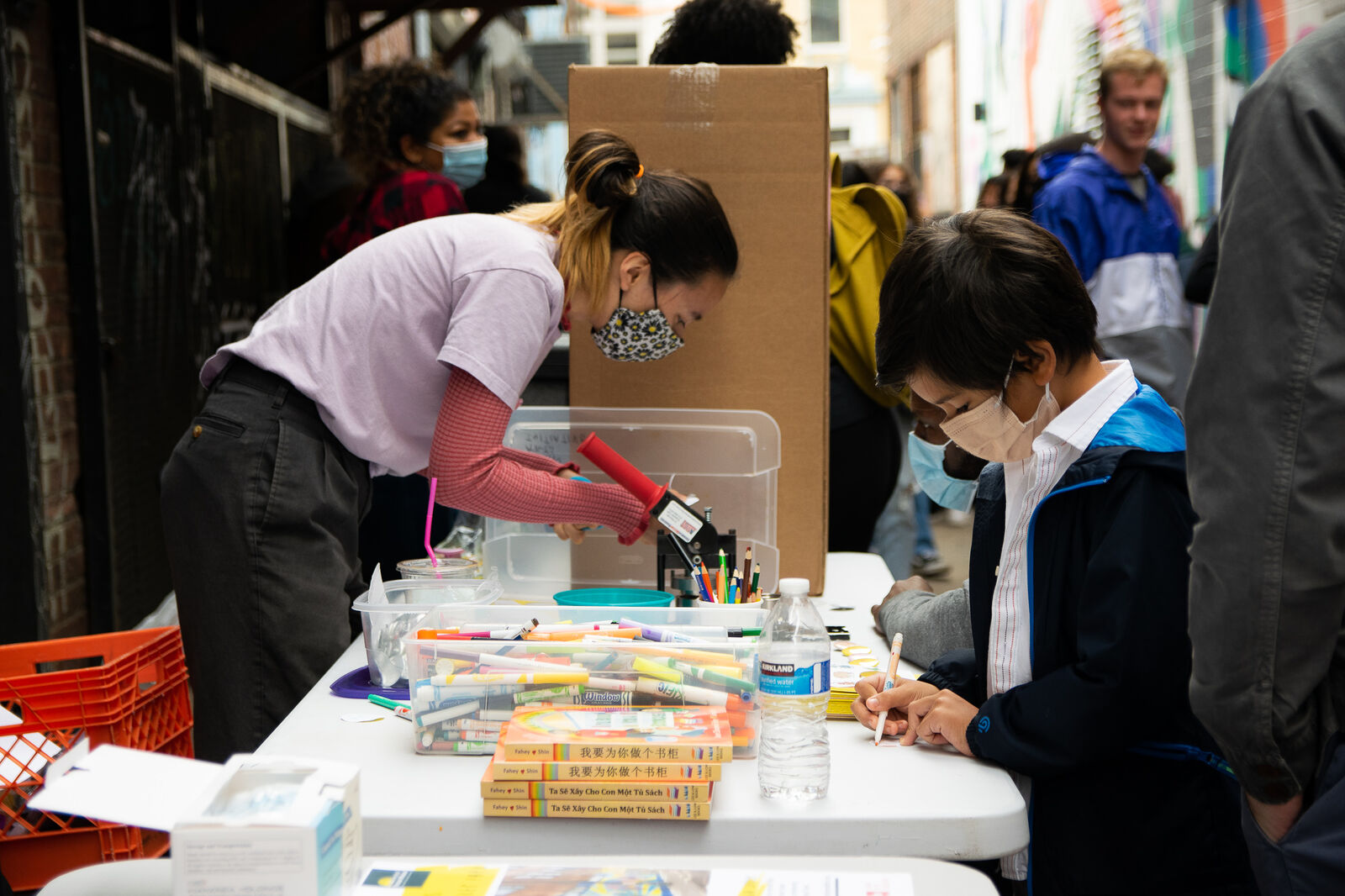 tow masked people draw at a table full of art supplies