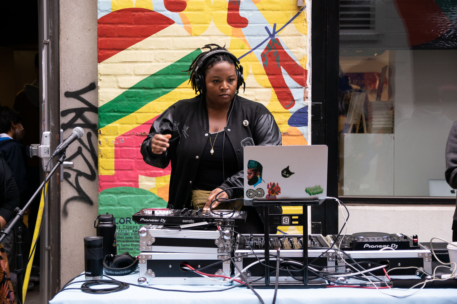 woman with short locks djs in front of colorful mural