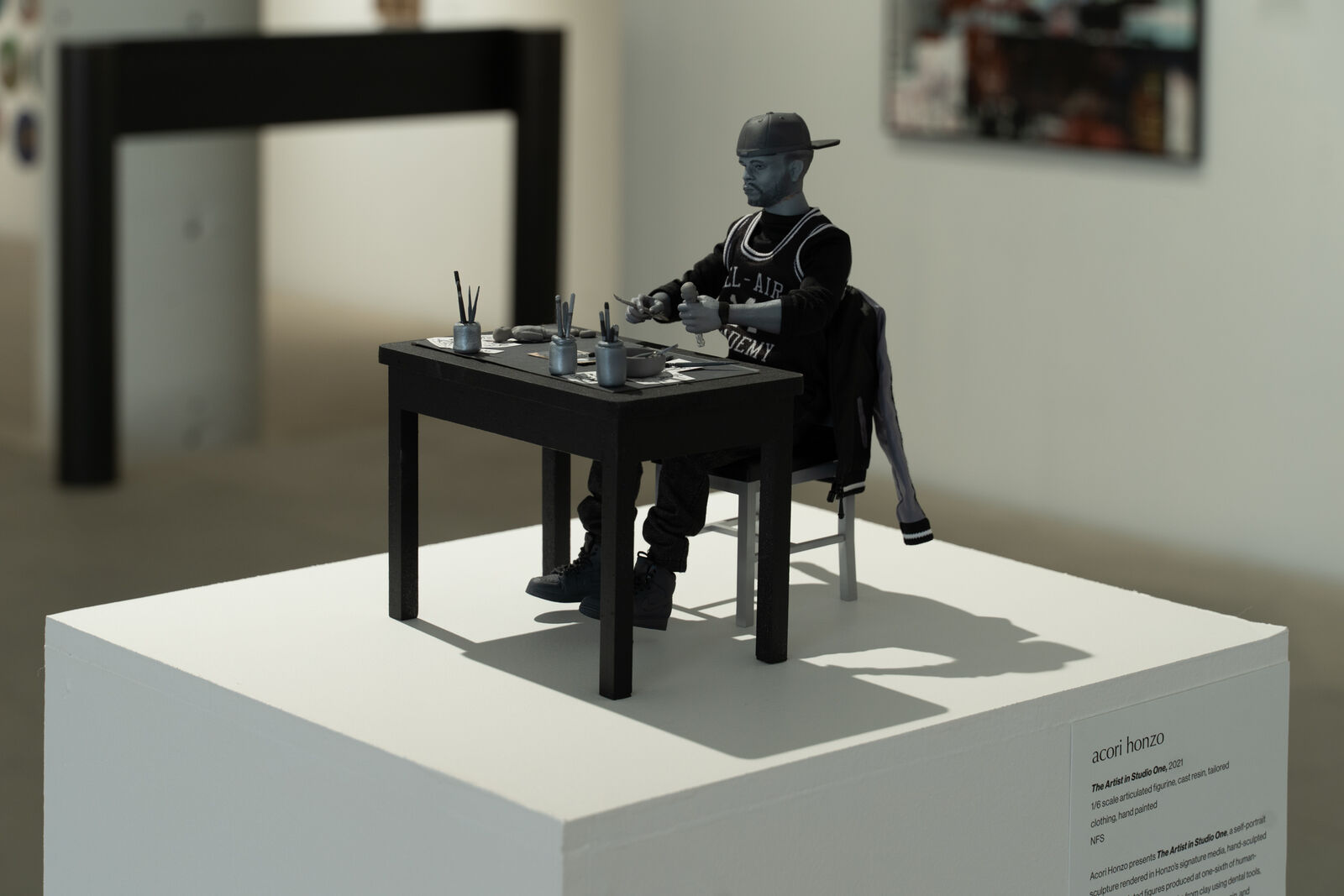 a miniature sculpture of a man seated creating art at a table sits on a pedestal
