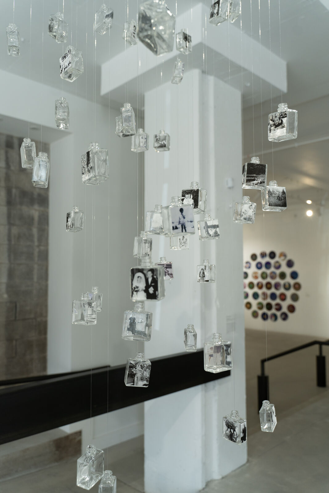 glass bottles with black and white pictues create a textured mobile that hangs from a gallery ceiling