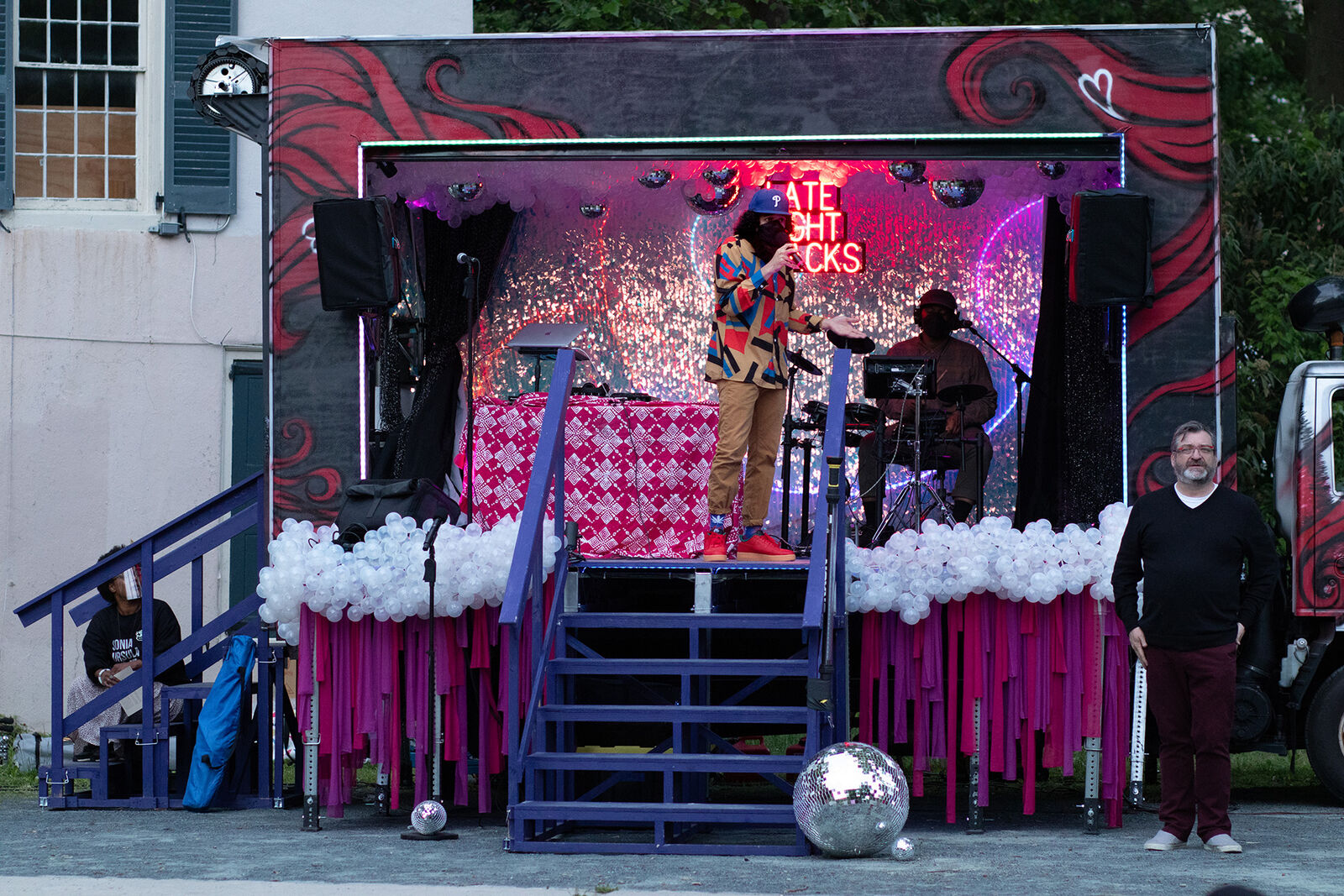 a stage covered in balloons and disco balls and pink lights hosts a person MCing an event with an ASL interpreter below