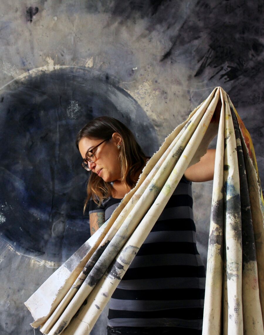 woman folding large canvas in front large atmospheric painting