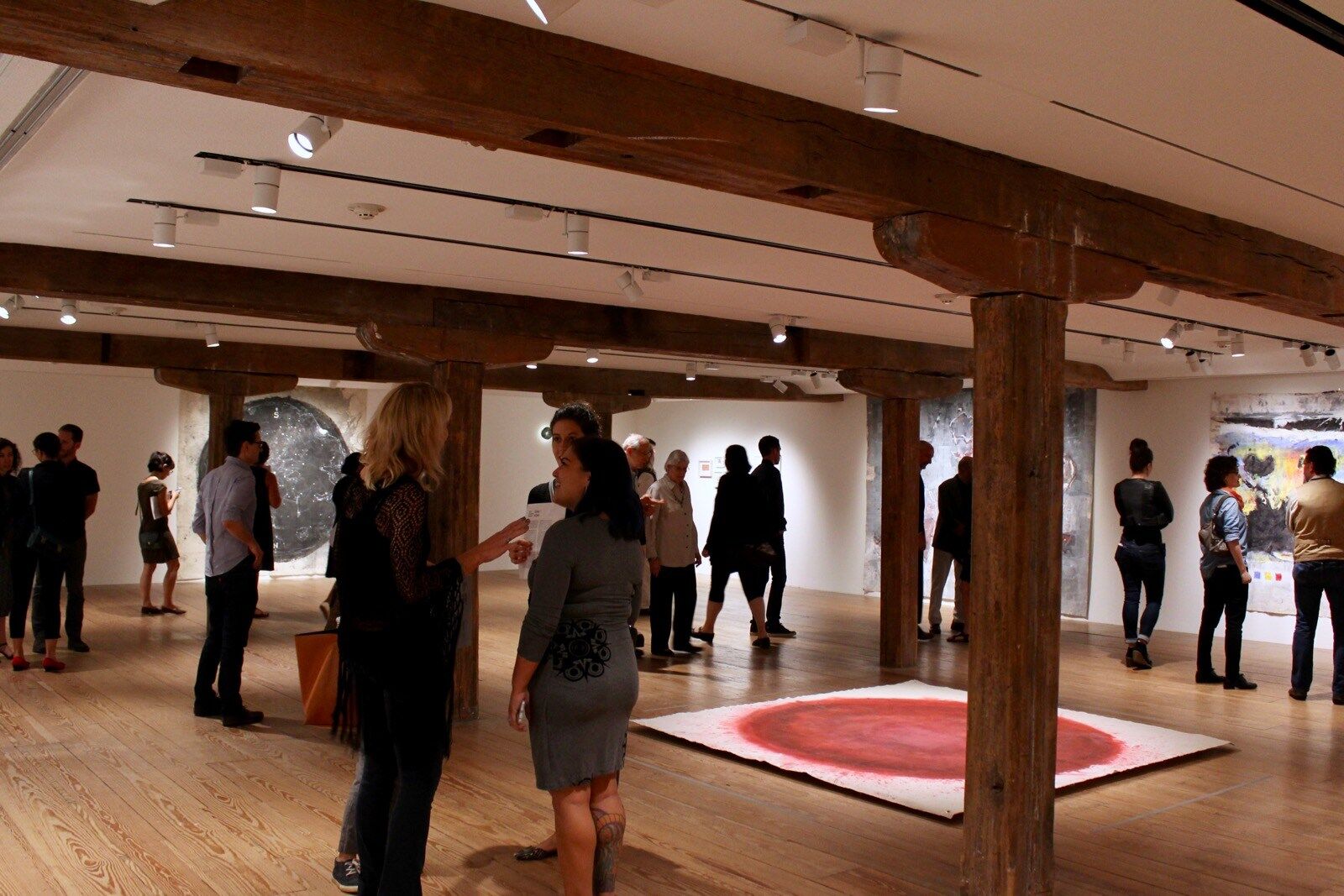 people gather in a gallery with large atmospheric paintings covering the wall and the floors