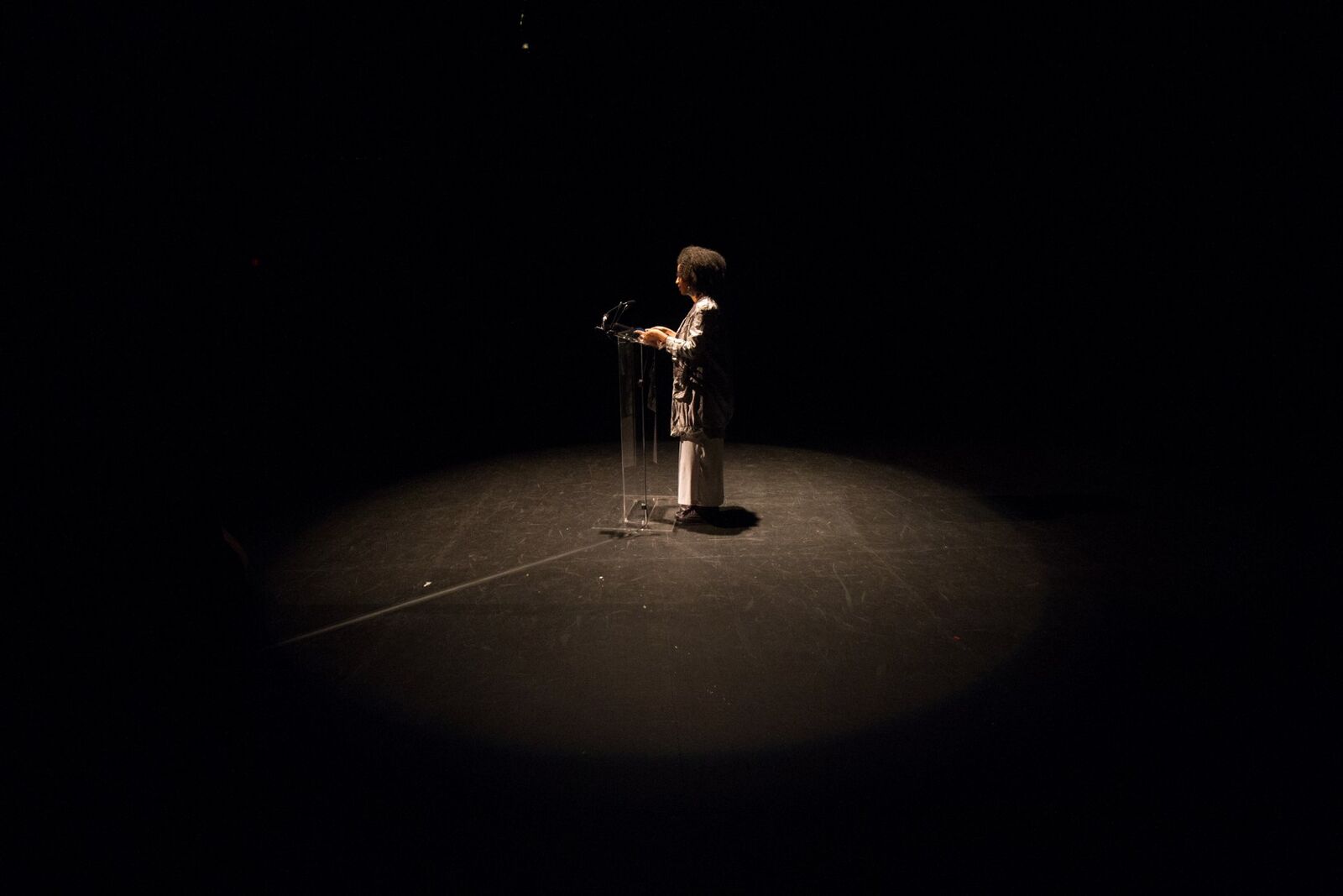 person stands at a podium with the spotlight on them, the rest of the room is black