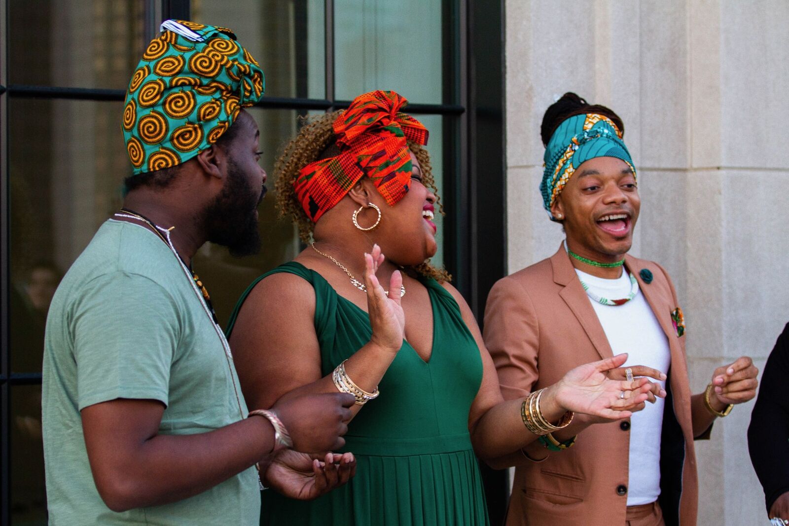 three people in head wraps smile and sing joyously