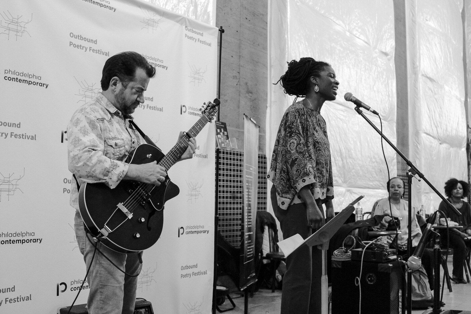 woman sings at a mic while man plays guitar next to her