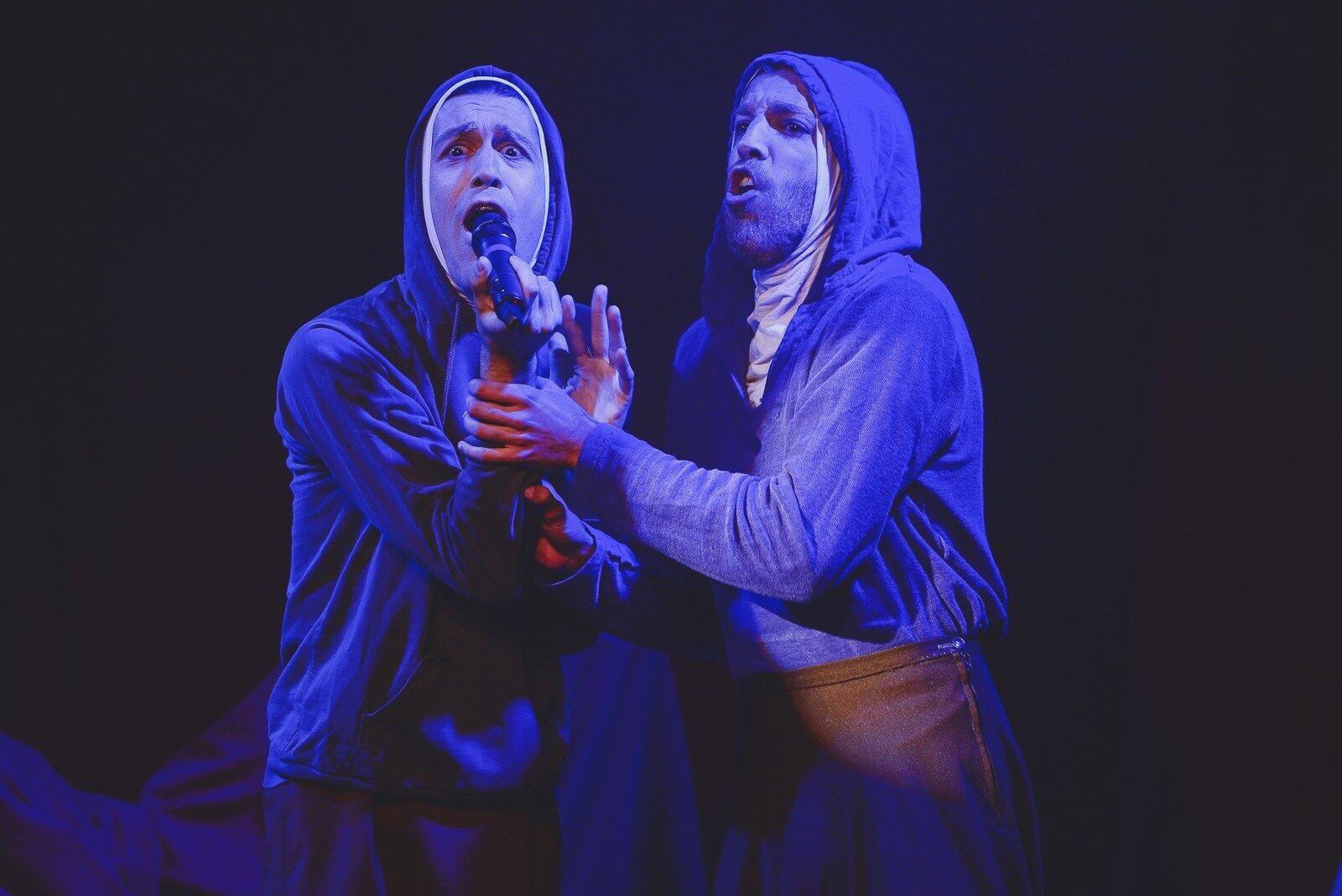 two men looking distressed a lit by blue light and speak in microphones wearing robes