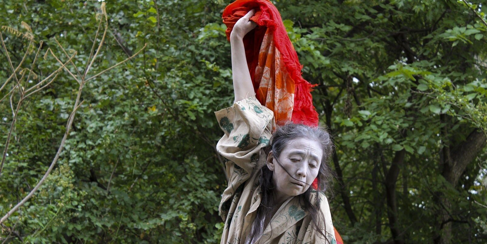 woman with red cloth dances in front of trees