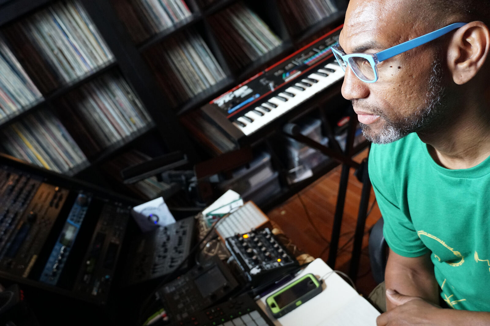 man sits in front of wall of vinyl records and keyboard staring out the window