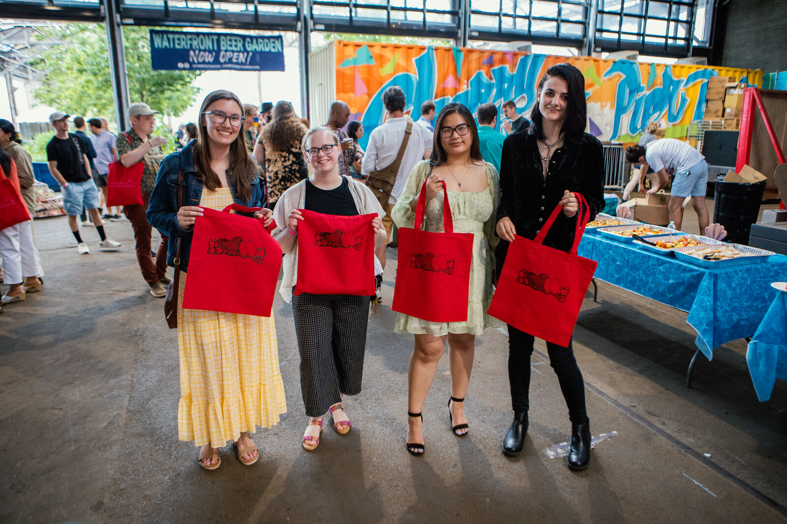 Four guests showcase red tote bags that they've screen-printed with a special illustration created for the event