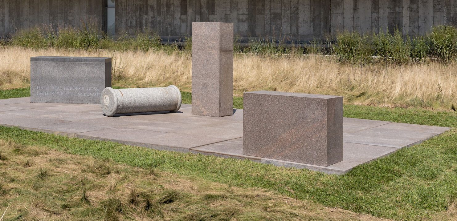 Four stone objects lay on a concrete slab in the midst of a grass field.