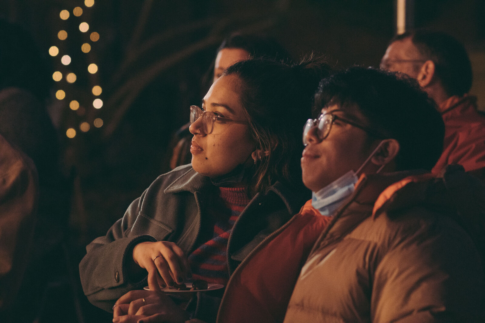 Two onlookers, a man and woman, both wearing eye glasses, glad in warm coats.