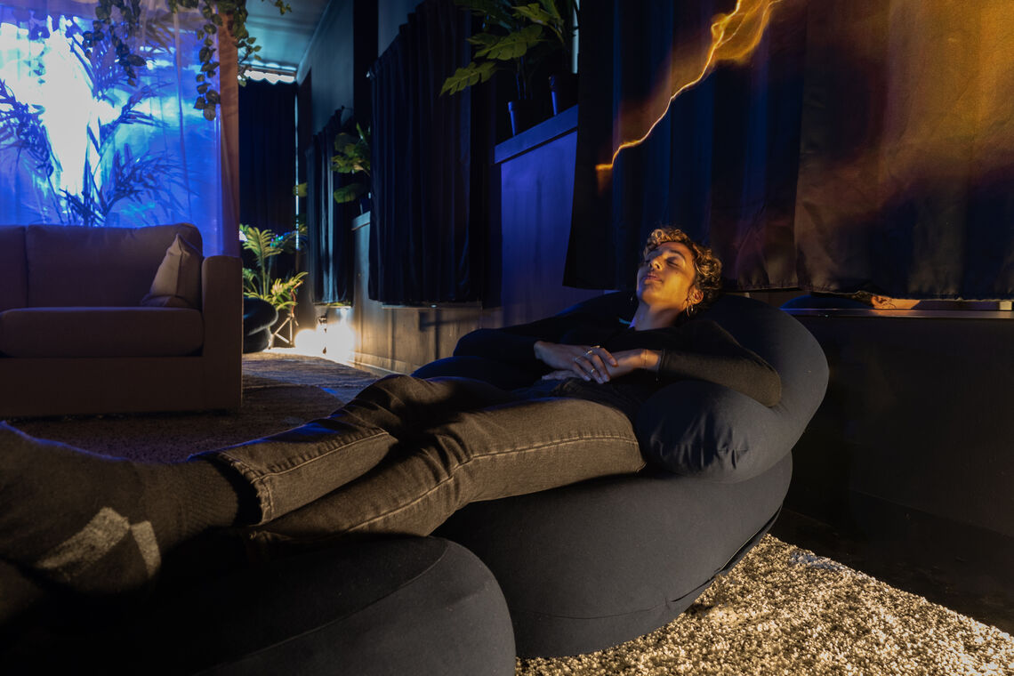 Curator Nicole Pollard lays on a dark bean bag chair, legs are propped up on a soft ottoman.